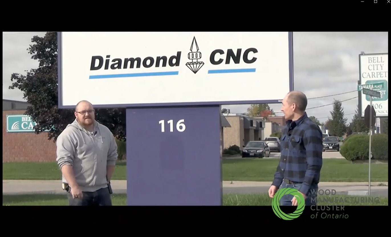 Rob Clare and Ryan Tabone stand outside on a cloudy day. They are standing next to a very large street sign that reads Diamond CNC